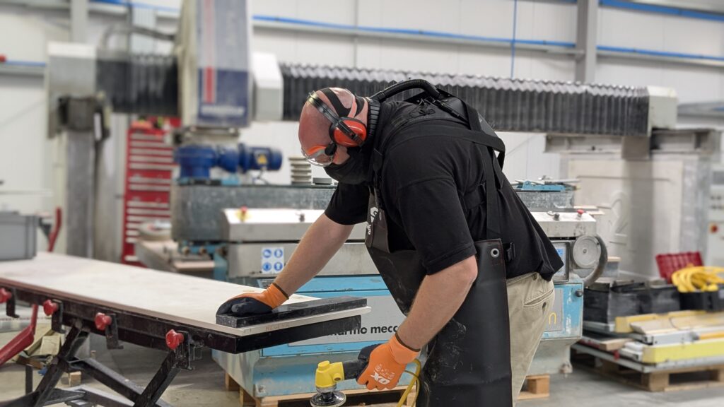 Stone fabricator in workshop with PPE including Optrel Swiss Air Respirator, gloves, ear defenders and safety goggles