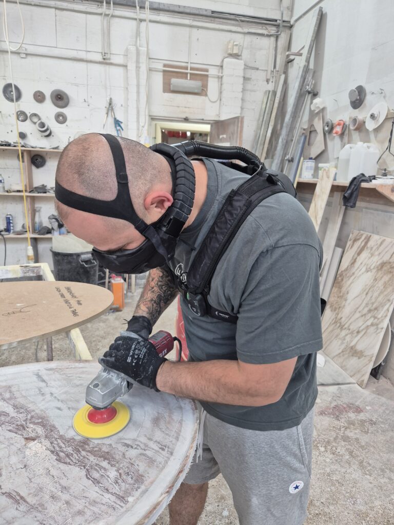 stone fabricator dry polishing a stone table with handheld polisher wearing Optrel Swiss Air respirator